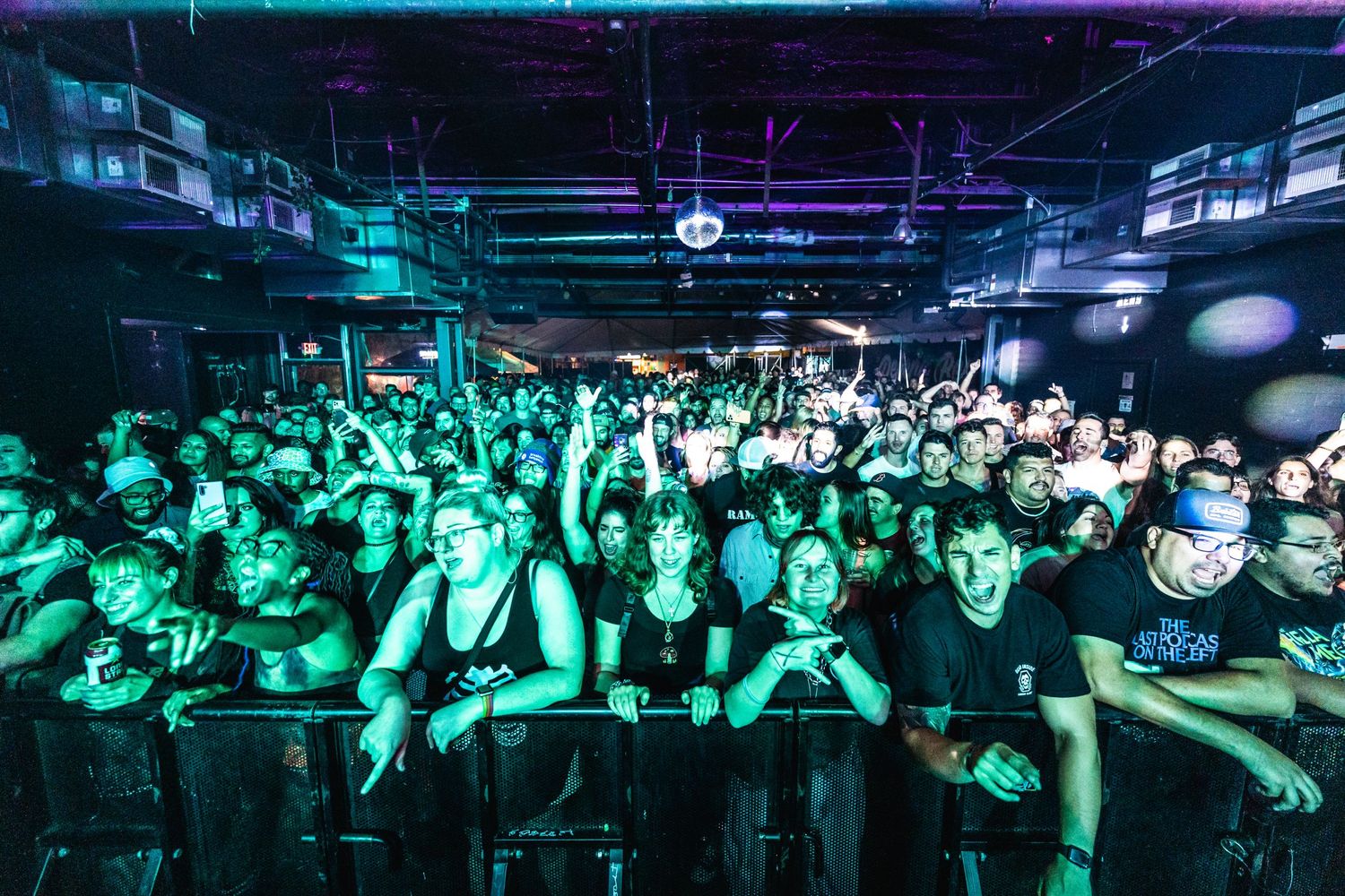 Crowded concert venue with enthusiastic audience bathed in green lighting.