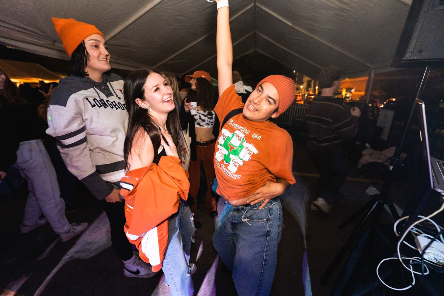 Energetic partygoers dancing and celebrating under a covered outdoor venue at night.