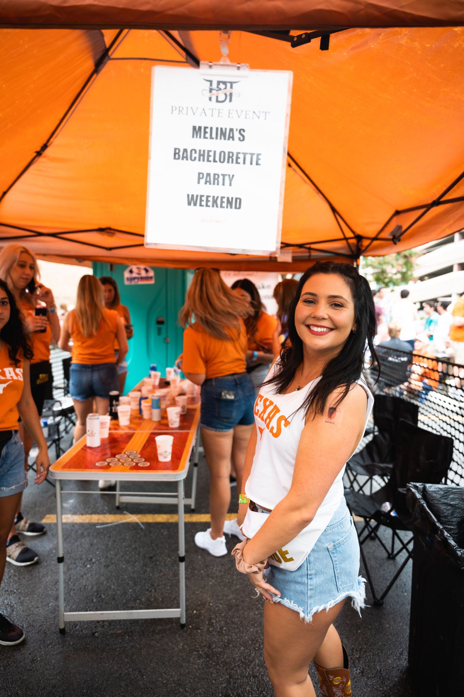 Bachelorette party celebration under orange tent with party sign visible.