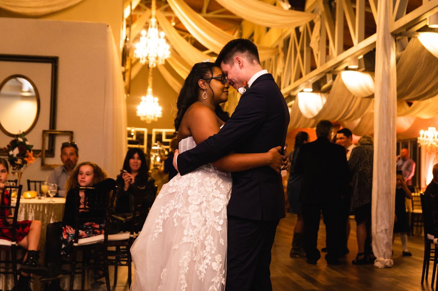A romantic first dance moment at a wedding reception under elegant draped fabric and chandeliers.