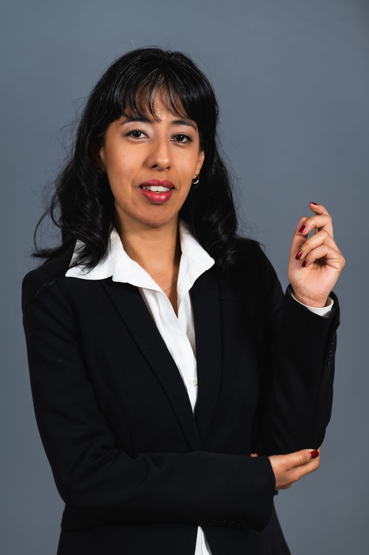 Business portrait of a woman in professional attire gesturing against grey backdrop.