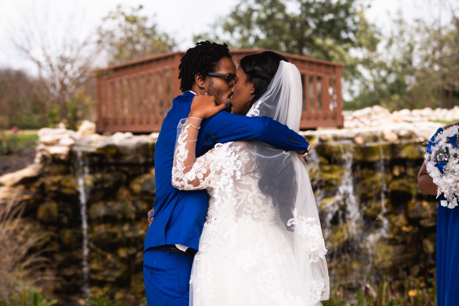A couple embraces during an outdoor wedding ceremony with a waterfall backdrop.