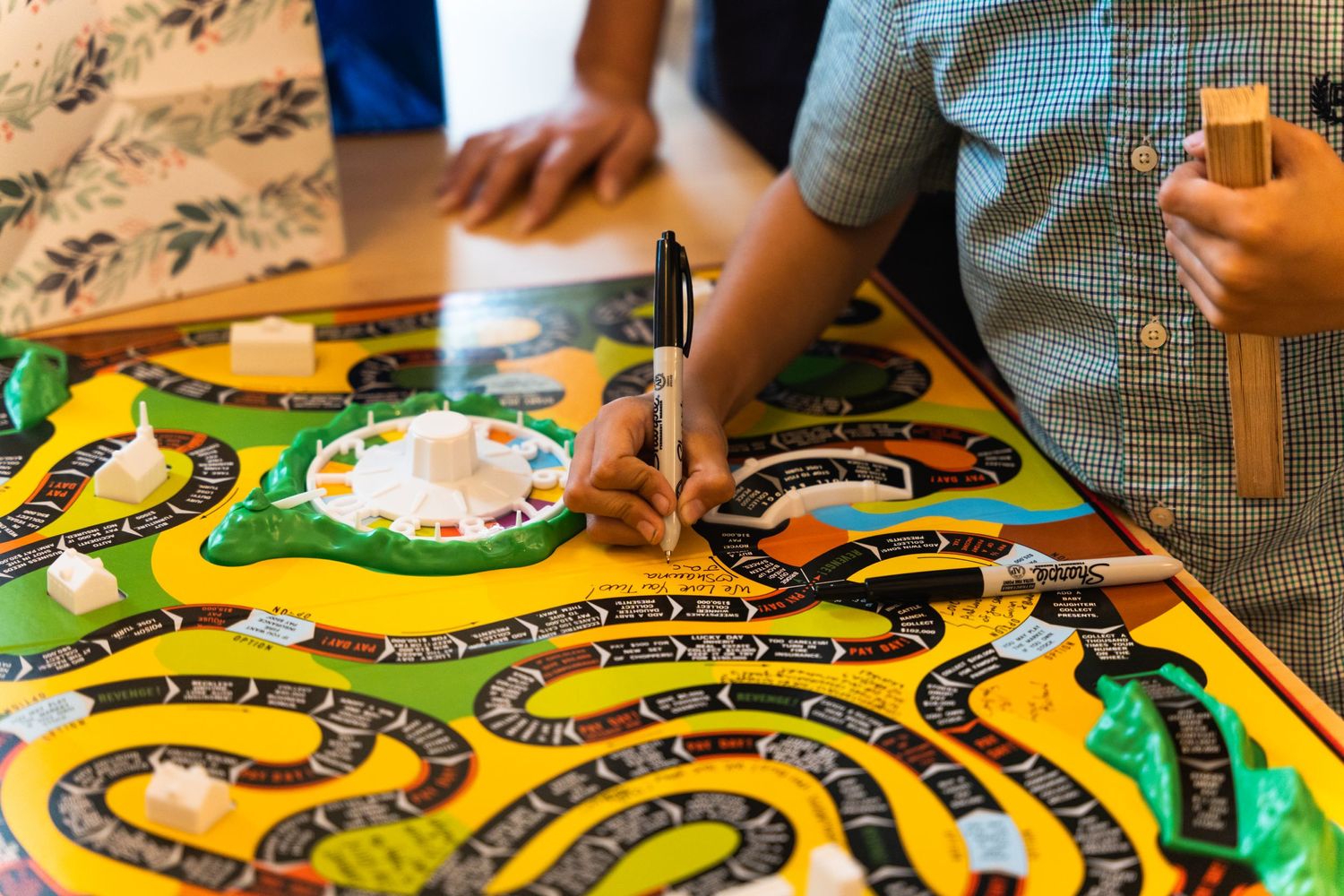 Hands moving pieces on a colorful board game with winding yellow paths.