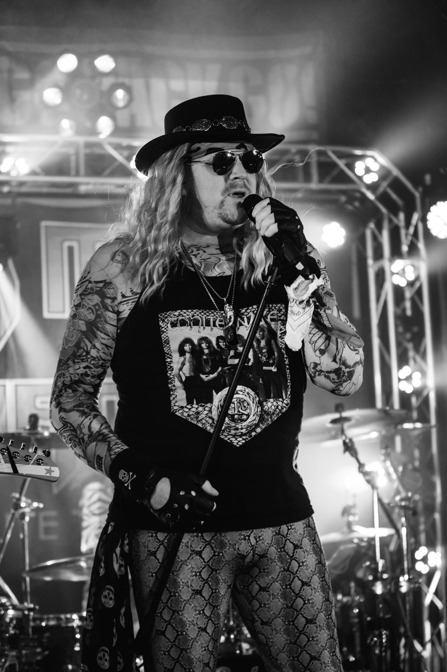 Rock vocalist performs in snakeskin pants and band shirt under concert spotlights.