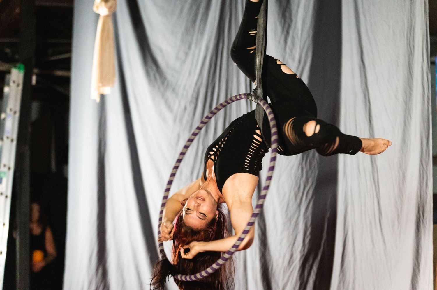 Performer executes graceful aerial hoop maneuver in dramatic lighting.