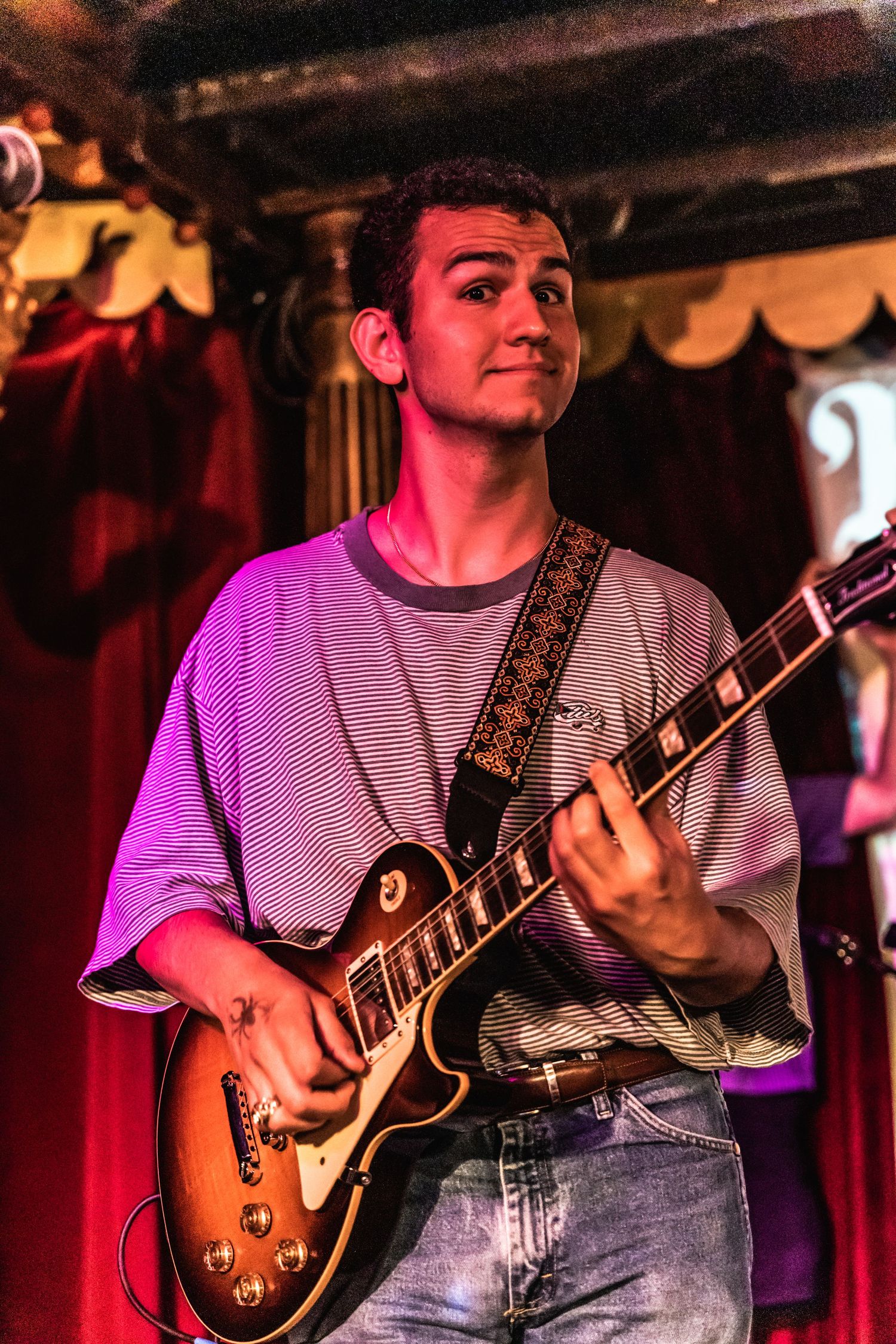 Musician playing electric guitar on stage under dramatic purple lighting.