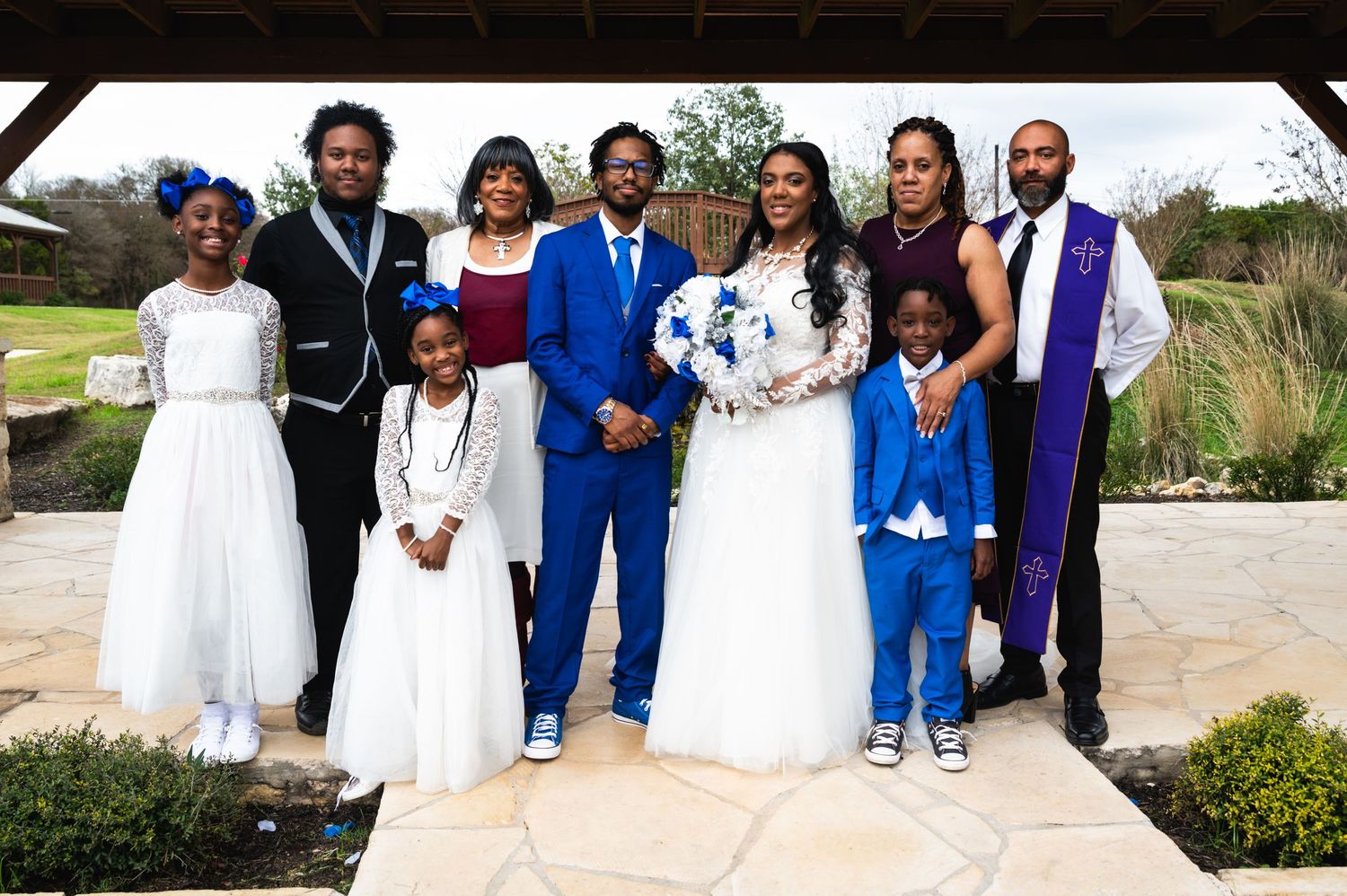 Wedding party poses together on stone path wearing coordinated blue, white and purple formal attire.