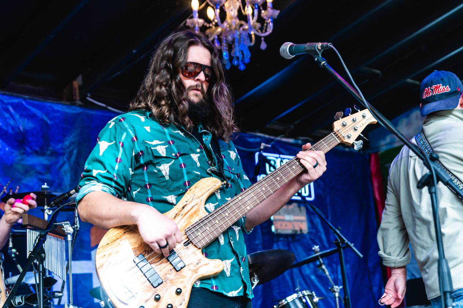 Bass guitarist in teal patterned shirt performs during live outdoor concert.