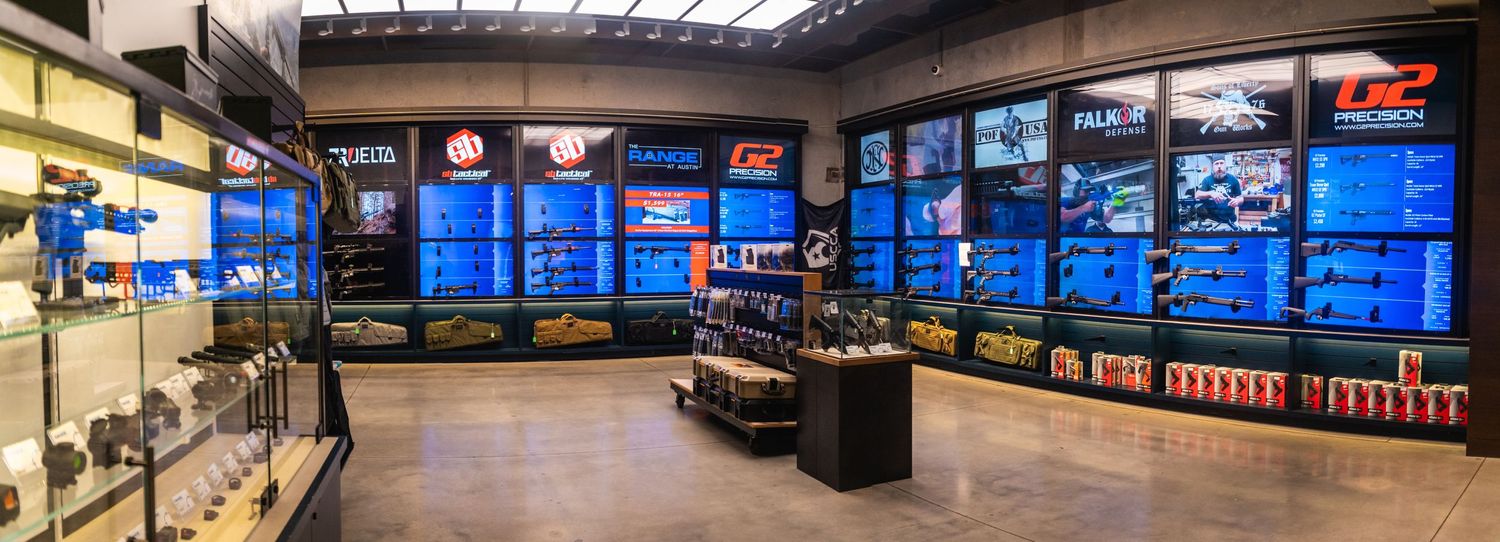 Modern shooting range retail space with multiple wall-mounted display screens and glass counters.