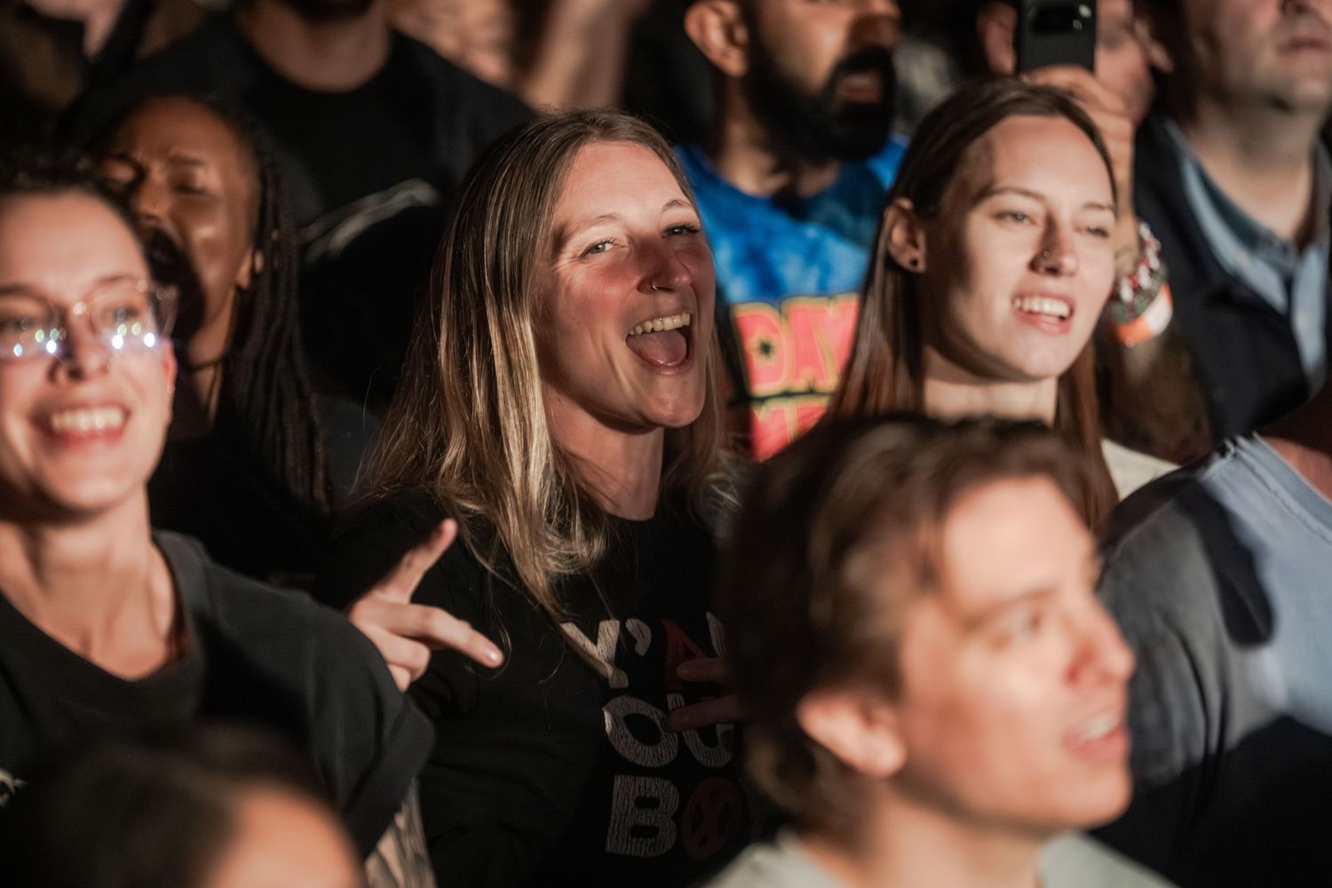 A crowd of people enjoying a concert or performance with blue lighting visible in the background.