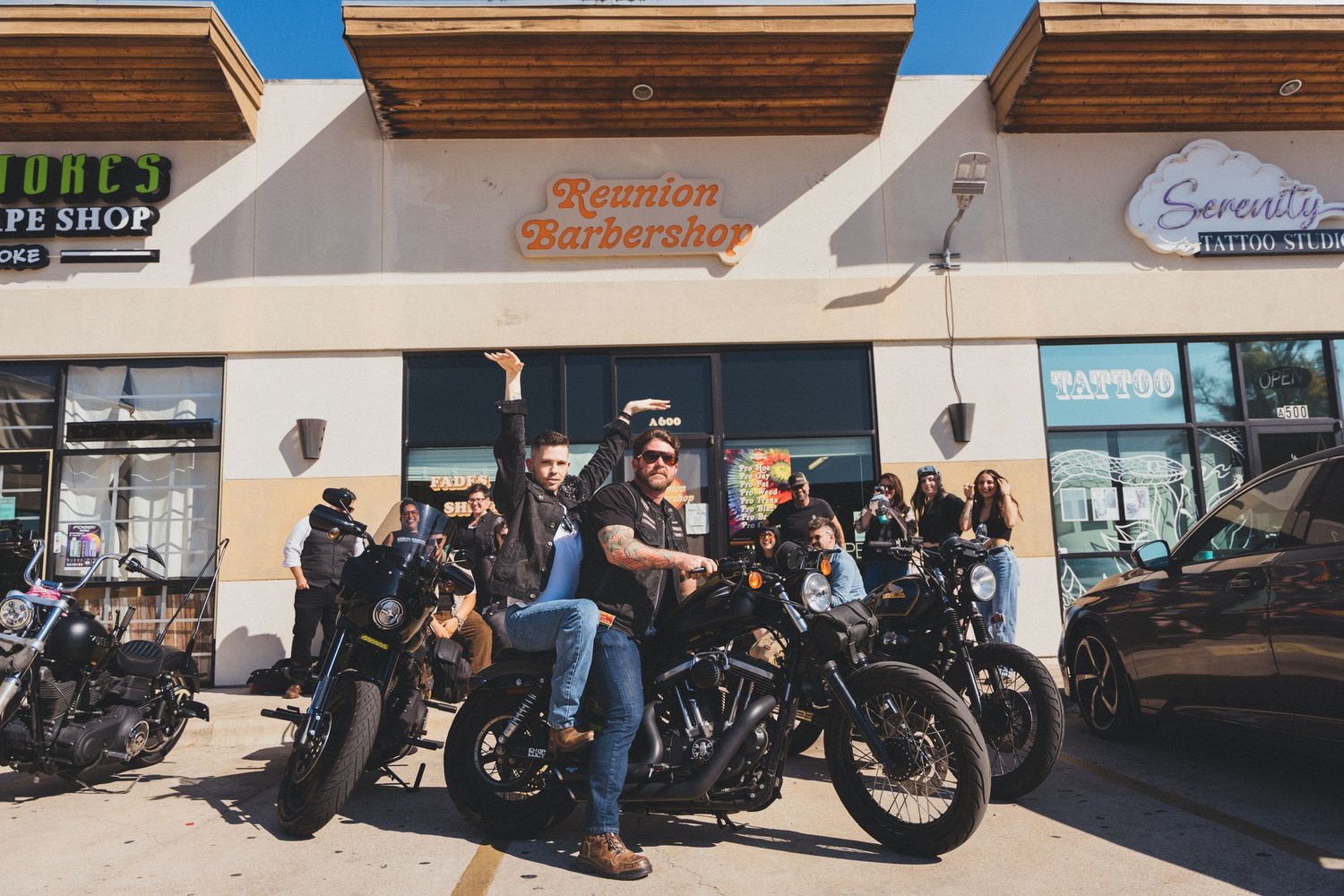 Custom motorcycles lined up outside a shop with blue sky and buildings in the background.