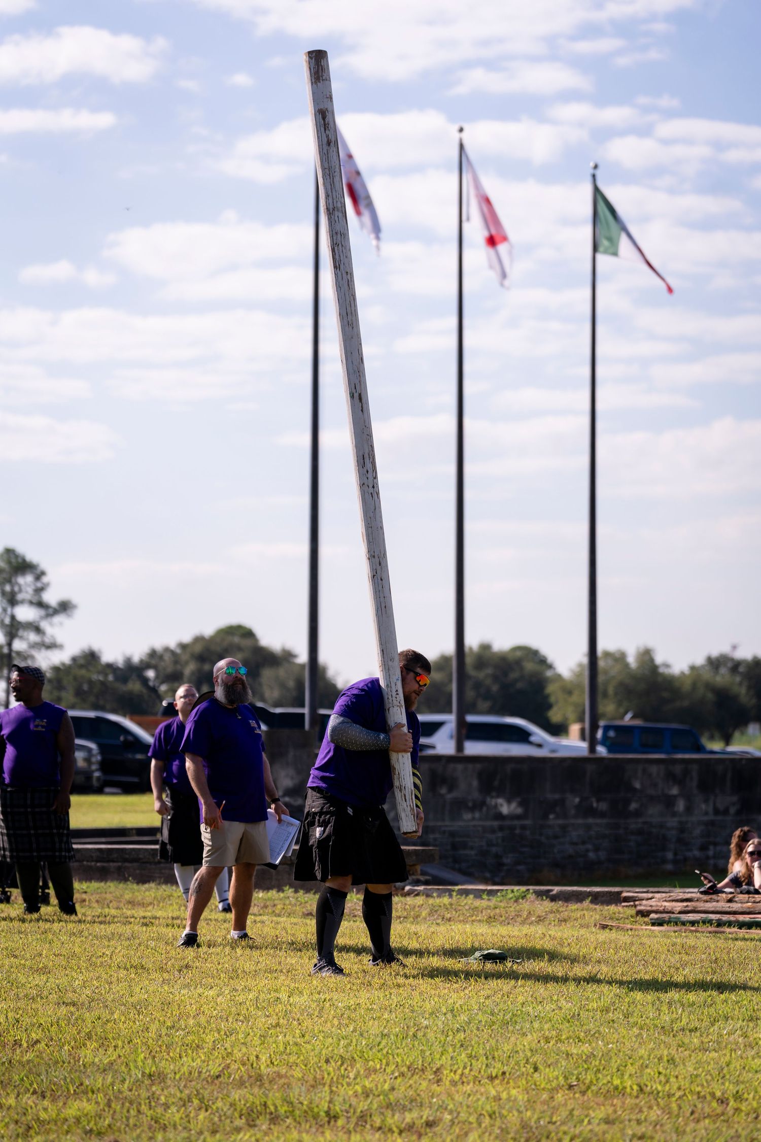 Several people gather on a grassy field with flags flying in the background on a sunny day.