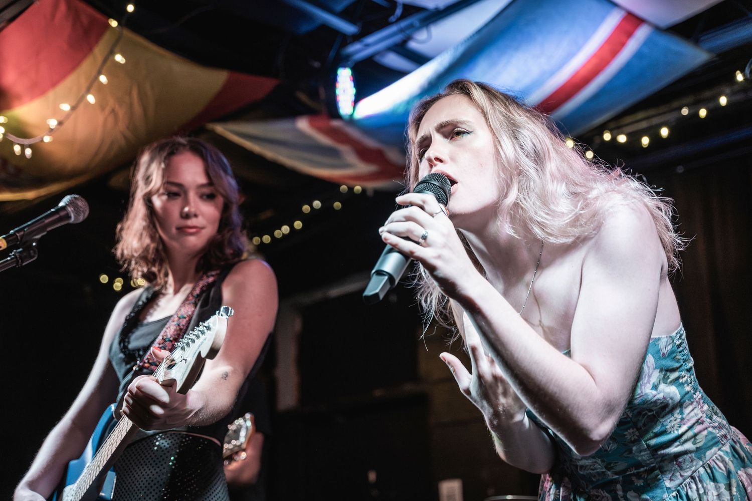 A performer in a teal dress sings passionately on stage under dramatic lighting during a live music performance.