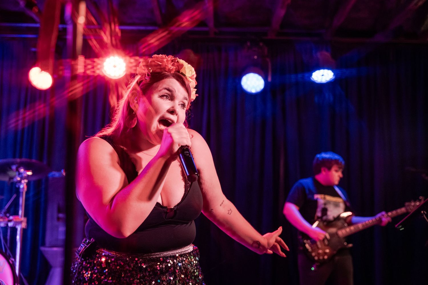 Musicians perform on stage with dramatic red and blue lighting effects at a concert venue.
