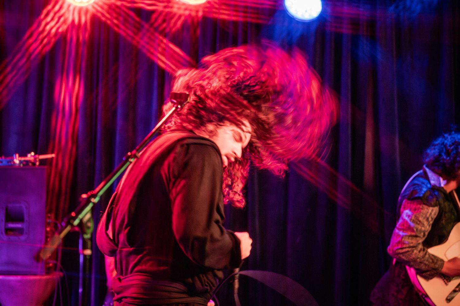 Concert performers on stage bathed in dramatic red and blue lighting during an energetic live music performance.
