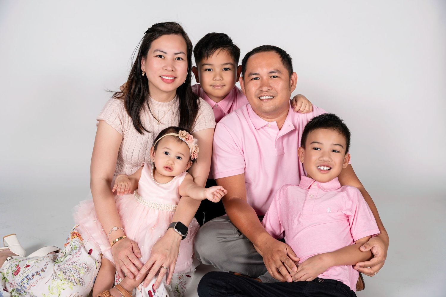 Happy Asian family of five posing together in matching pink outfits for a professional studio portrait photo.