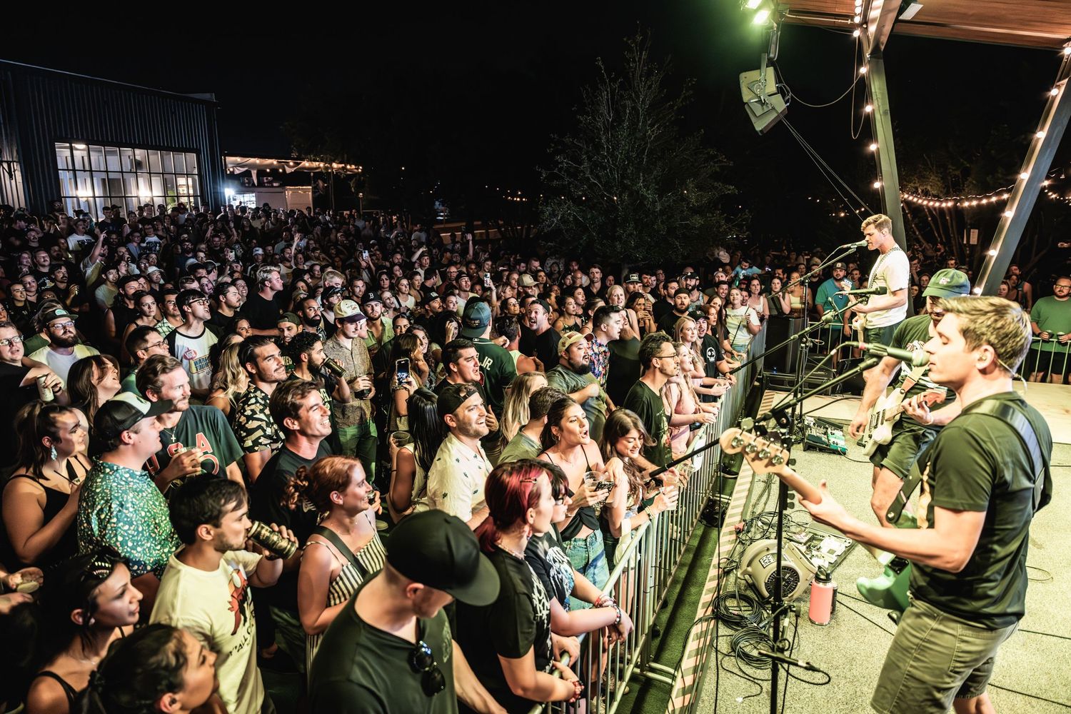 Large crowd watches performers on stage at an outdoor nighttime concert venue.