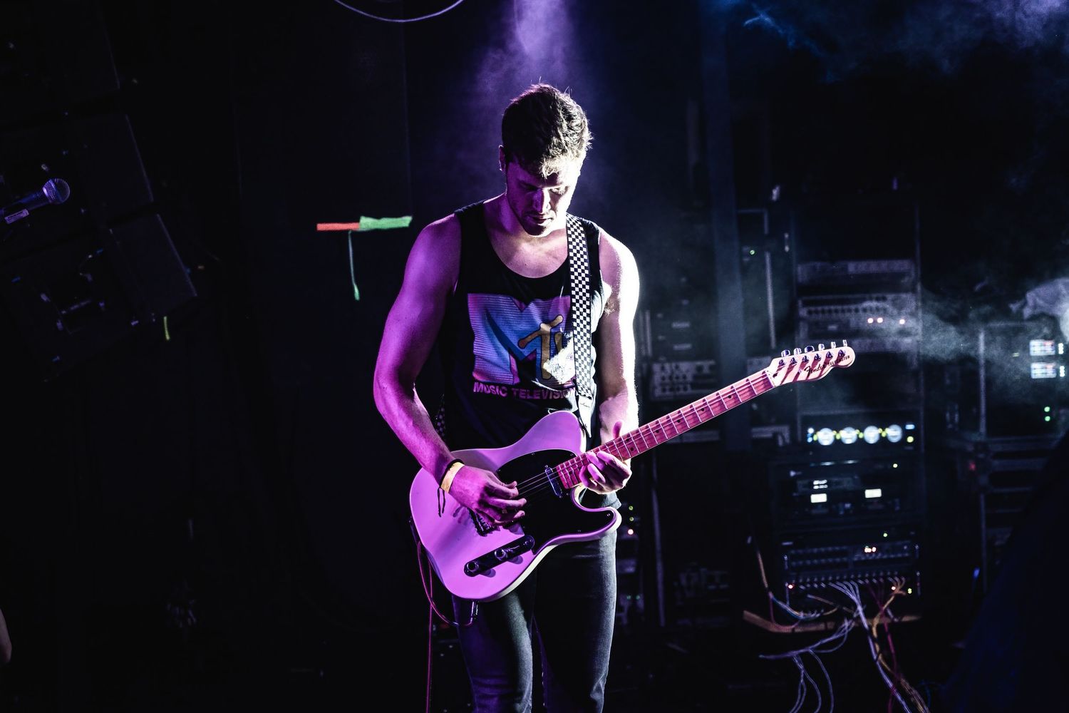 Guitarist performs on stage bathed in purple lighting during a live concert performance.