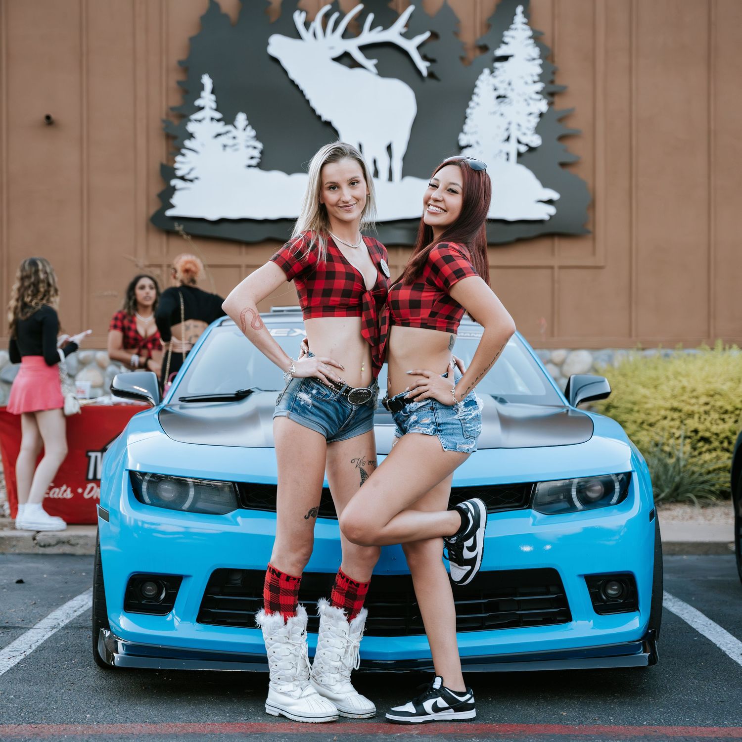 Casual car meet photoshoot featuring matching outfits against rustic wall art.