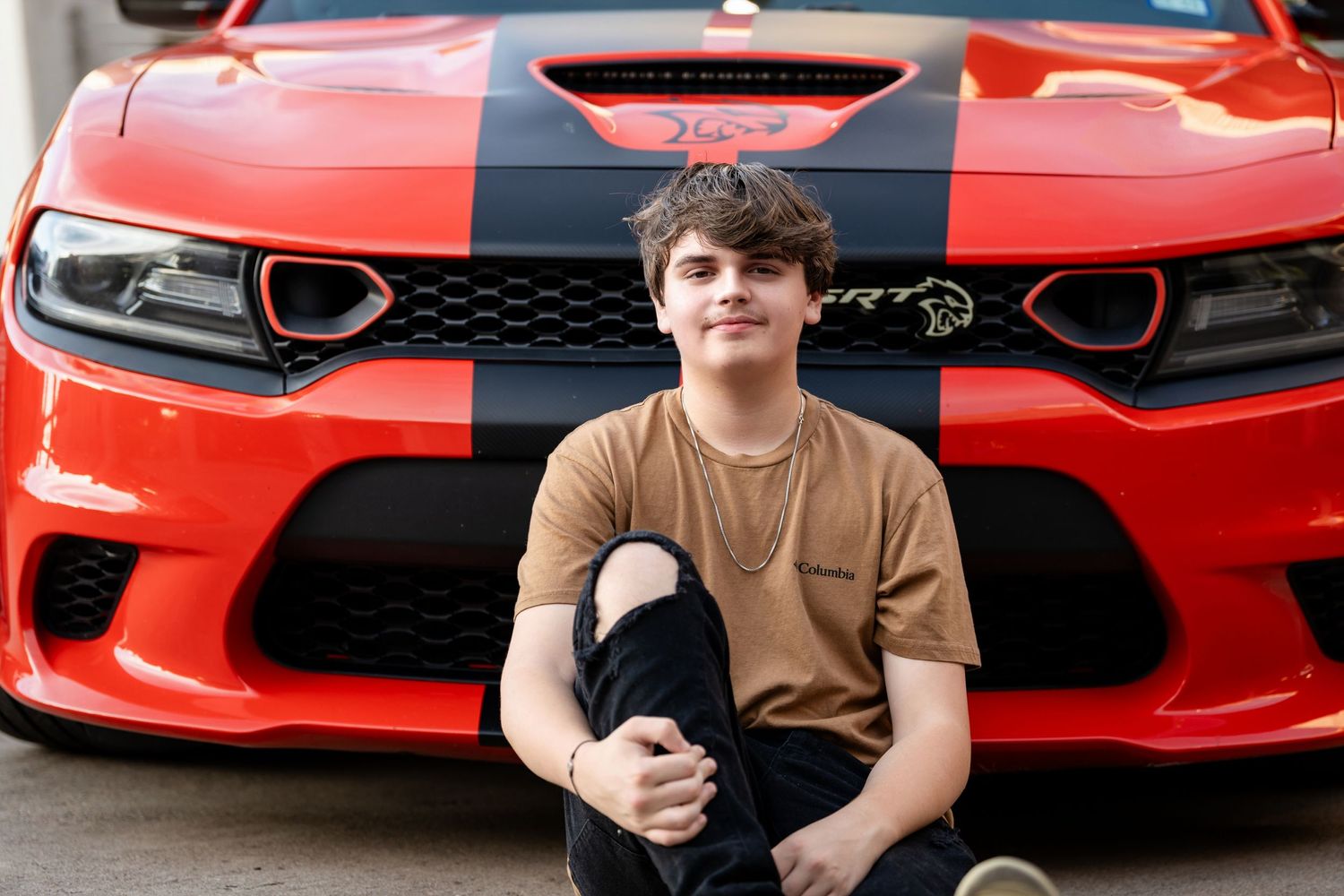 A close-up portrait against the grille of a modified red Dodge Charger SRT.