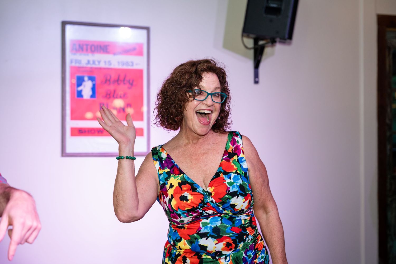 Woman in a colorful floral dress gesturing enthusiastically during an indoor event.