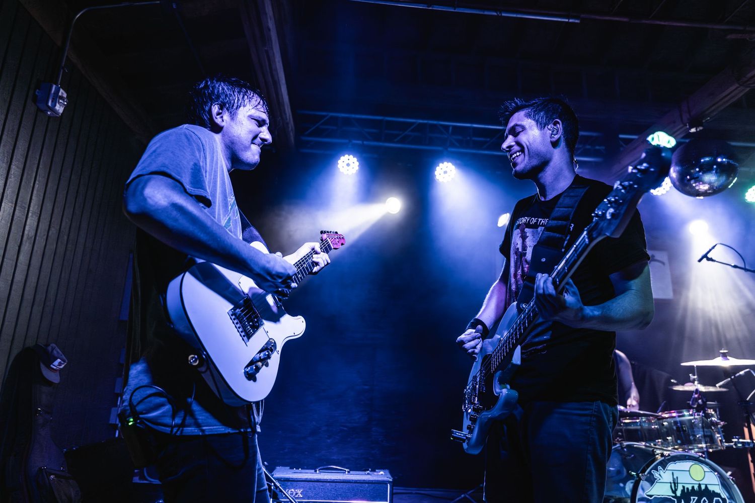 Two musicians performing on stage with guitars under dramatic blue lighting.