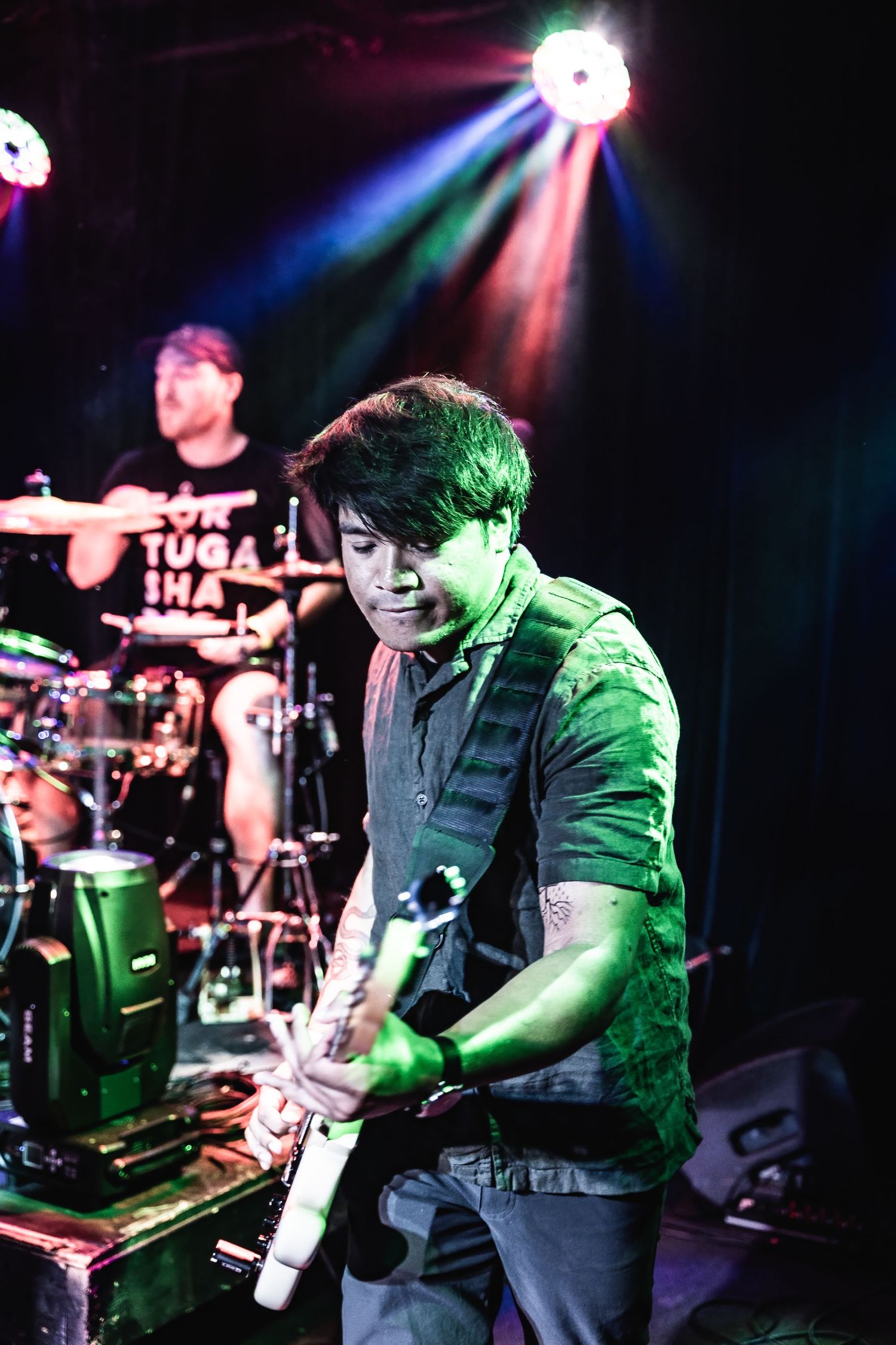 Musician plays guitar under green and red stage lighting during live performance.