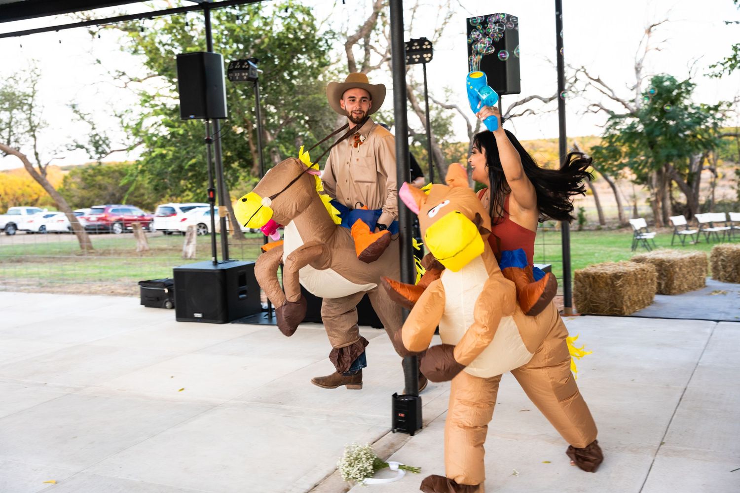 Performers in inflatable horse costumes dance at outdoor western-themed event.