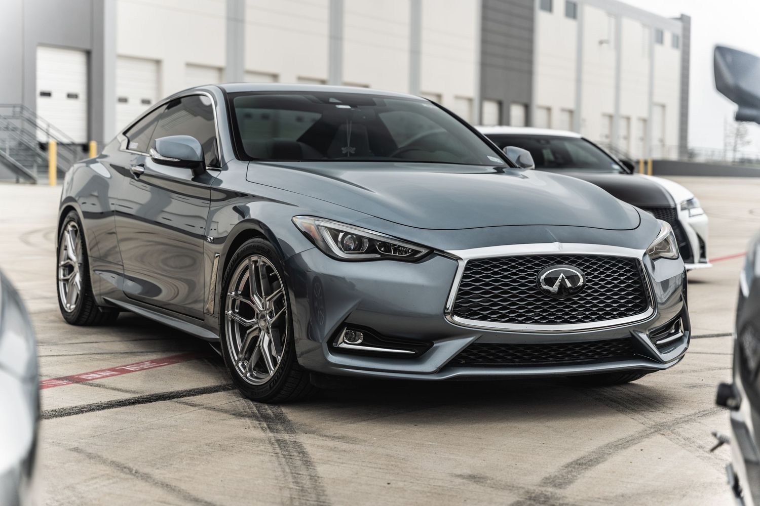 Silver Infiniti Q60 luxury sports coupe with sleek design parked in front of industrial building.