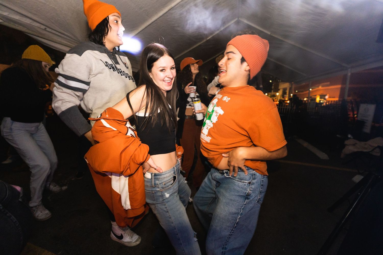 Group of people dancing and having fun at a tent party wearing orange and casual attire.