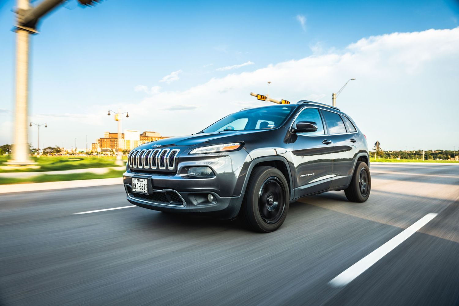 Gray Jeep Cherokee with black wheels driving on highway during daytime.