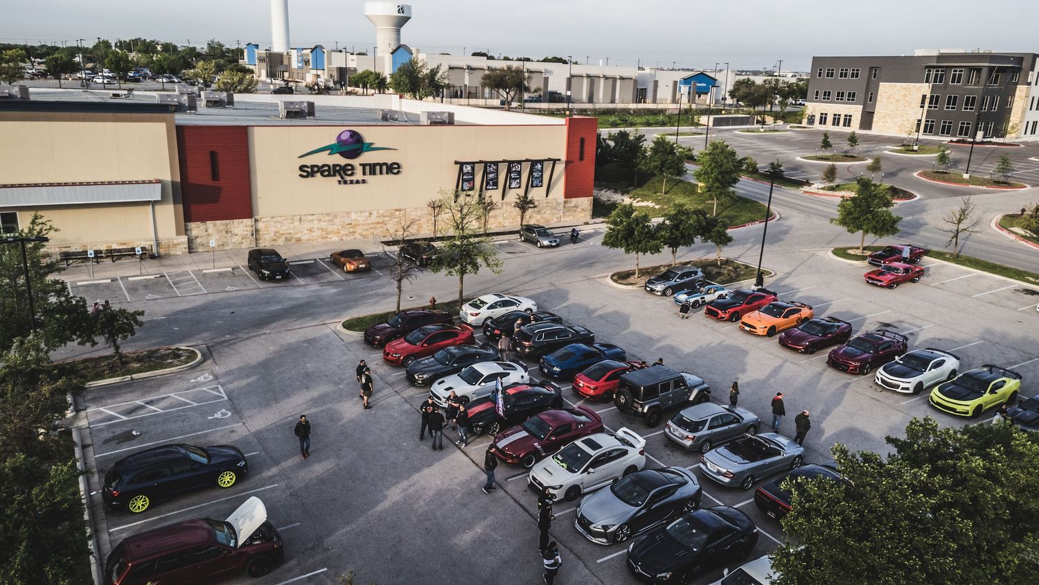 Aerial view of a parking lot filled with cars at a daytime car meet event.