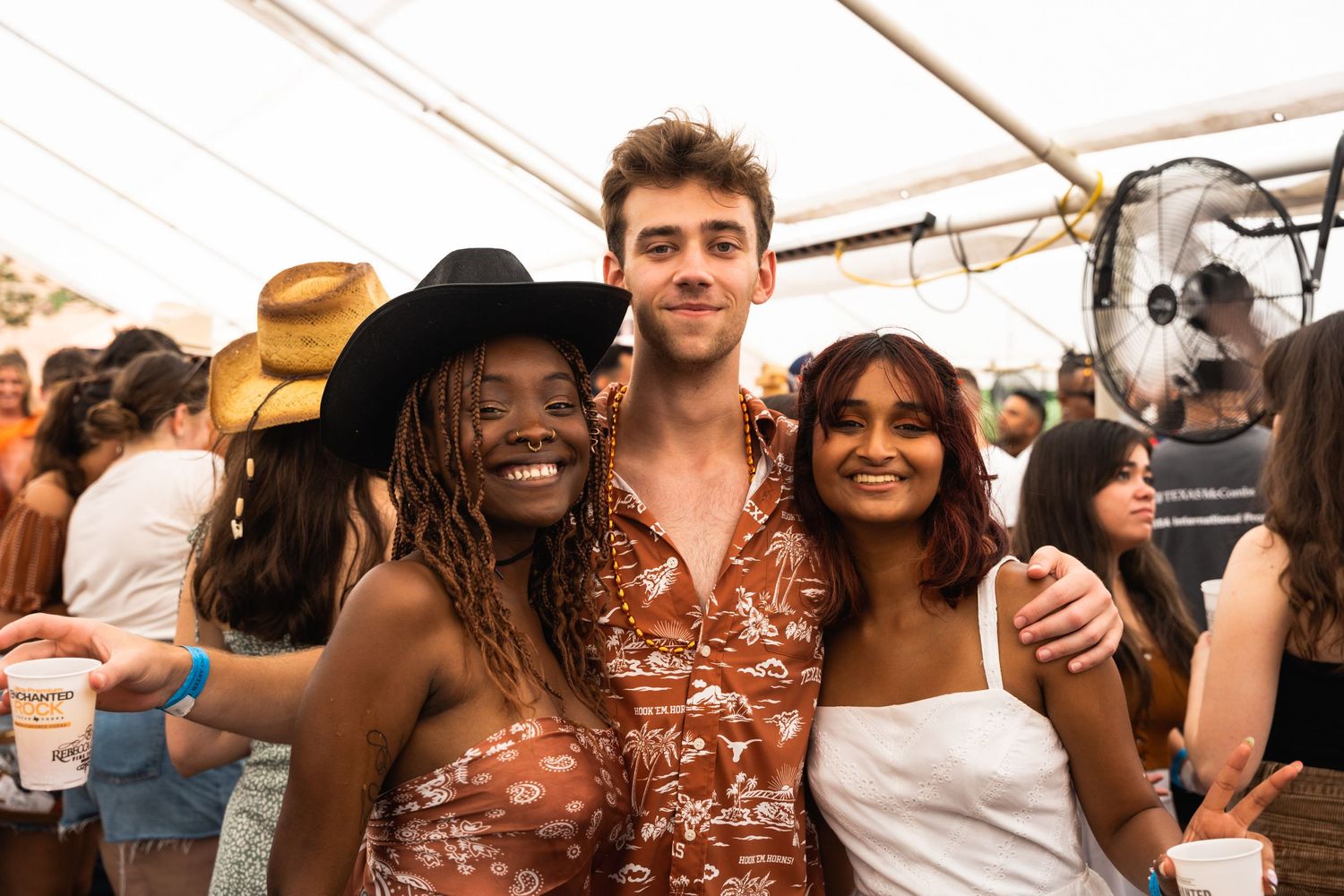 Three people in summer attire enjoying themselves at an outdoor festival.