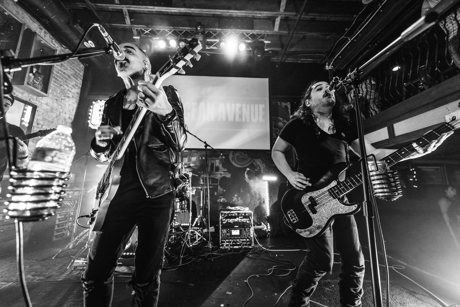 Black and white photo of two musicians performing energetically on stage with guitars.