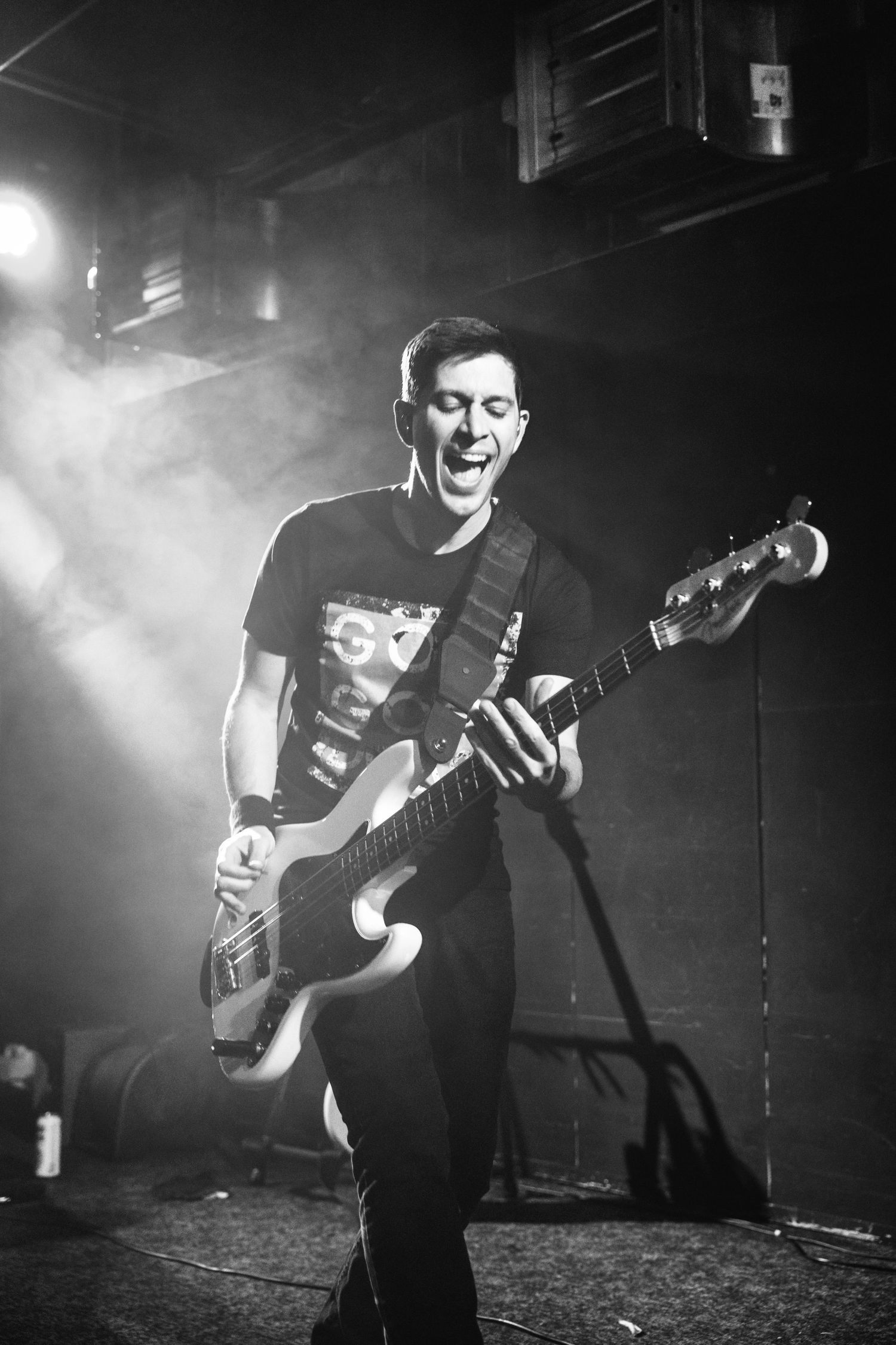 Musician plays bass guitar energetically on stage with dramatic smoke and lighting effects.