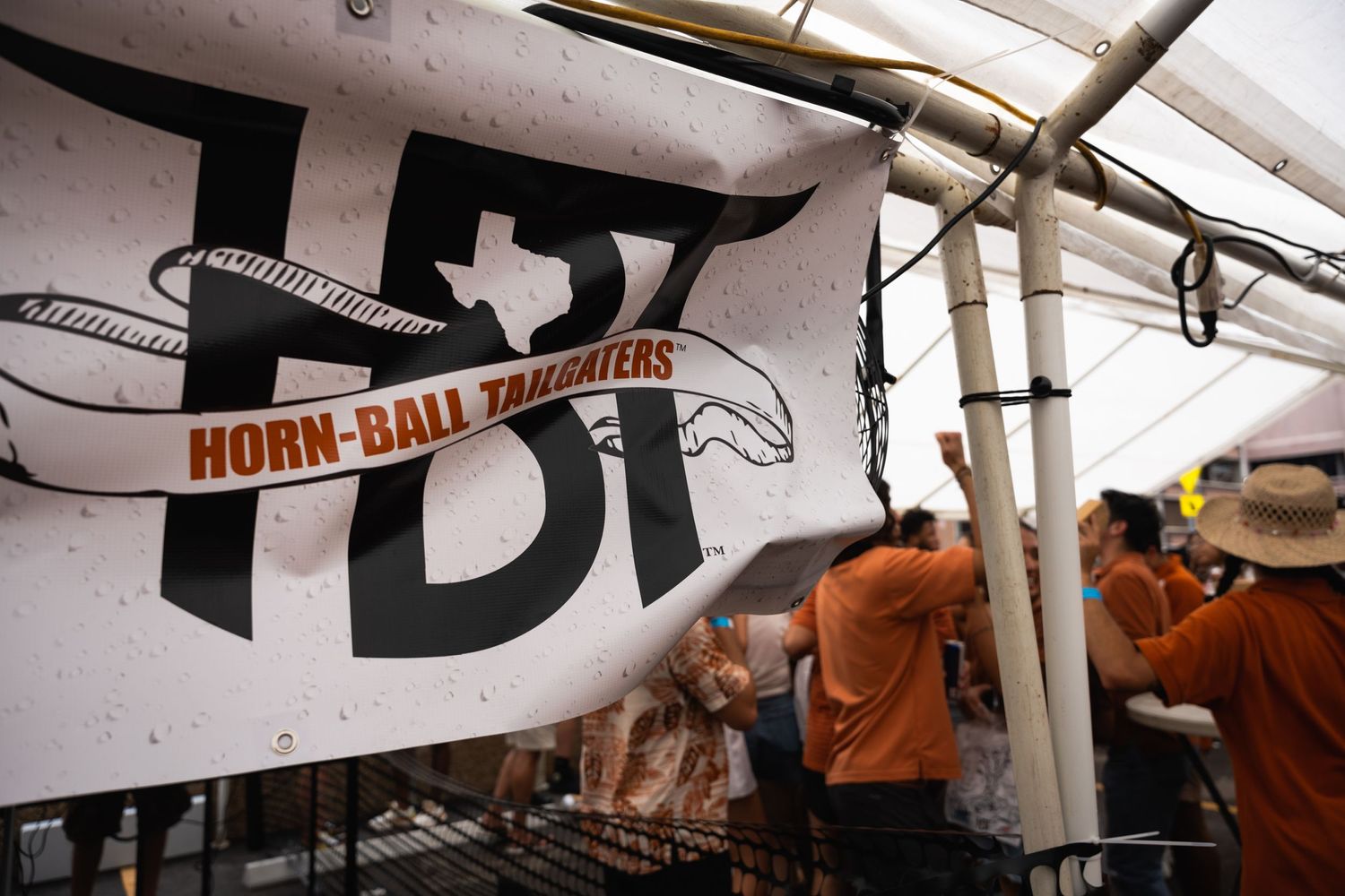 Horn-bat Texas banner hanging at an outdoor event tent with crowd visible below.