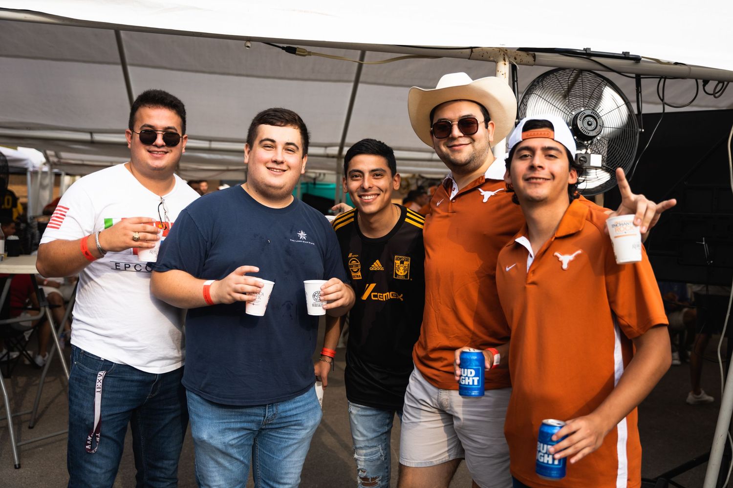 Group of sports fans in Texas orange and casual wear pose with drinks at outdoor gathering.