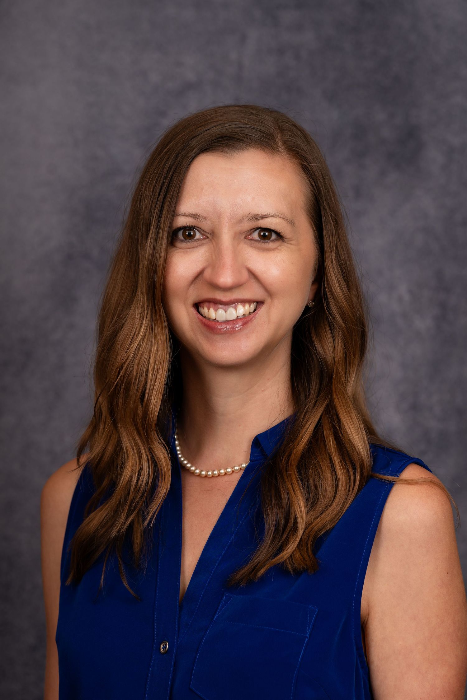 Professional portrait of person wearing navy blue sleeveless blouse and necklace.