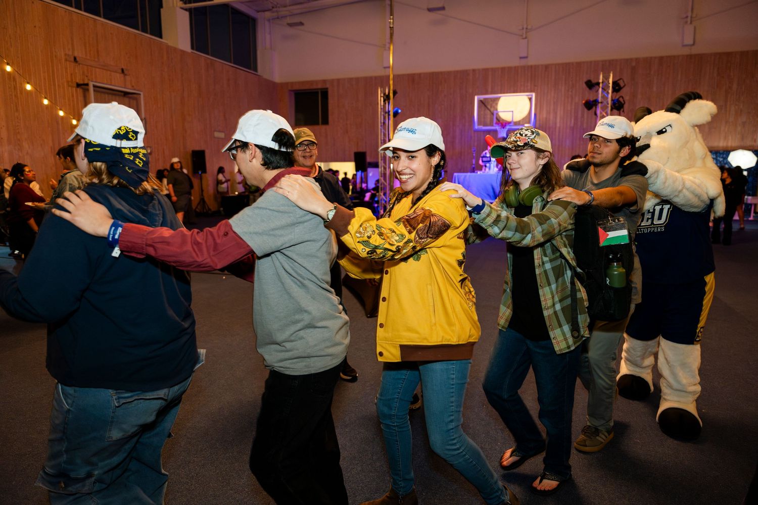 A group of people in casual winter wear dance together in a line formation at an indoor venue.