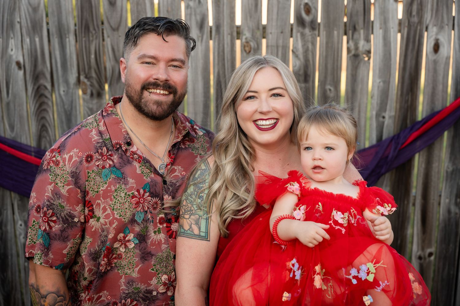 A family in coordinating red outfits poses together in front of a wooden fence.