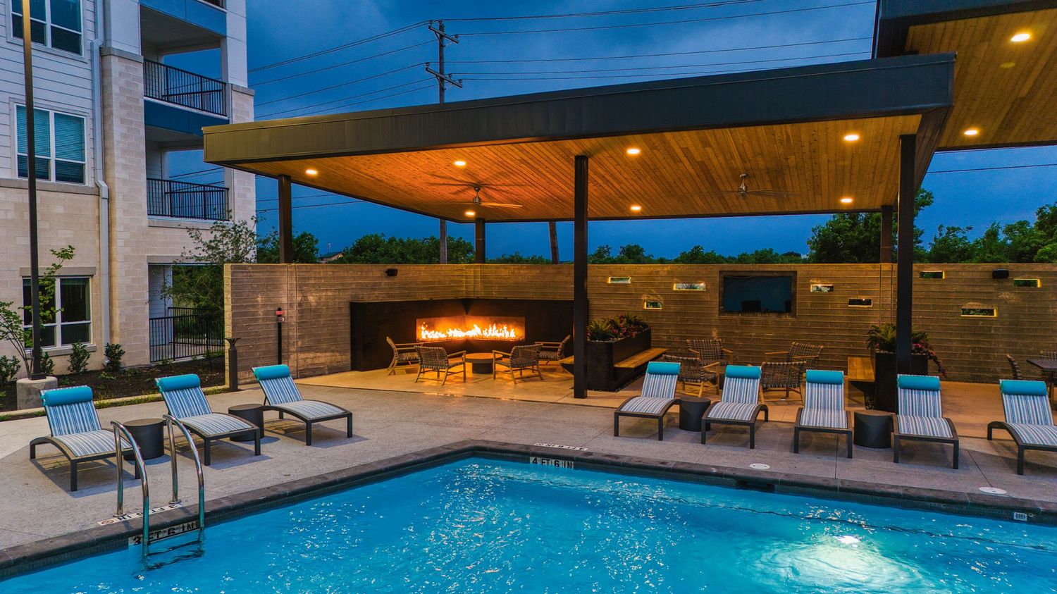 Resort-style pool area with covered lounge seating and outdoor fireplace at dusk.