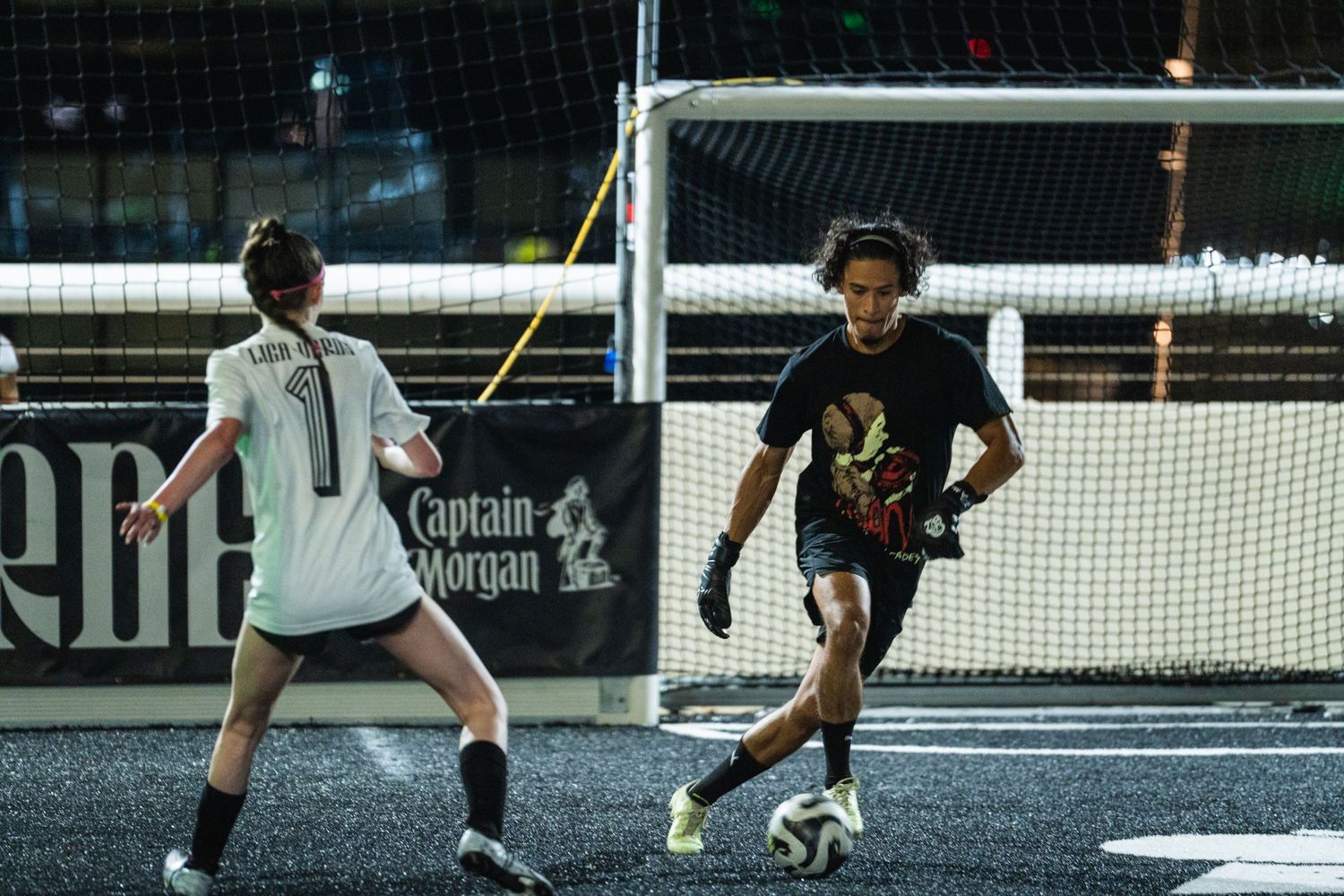 Two players compete in an intense indoor soccer match with a net barrier in the background.