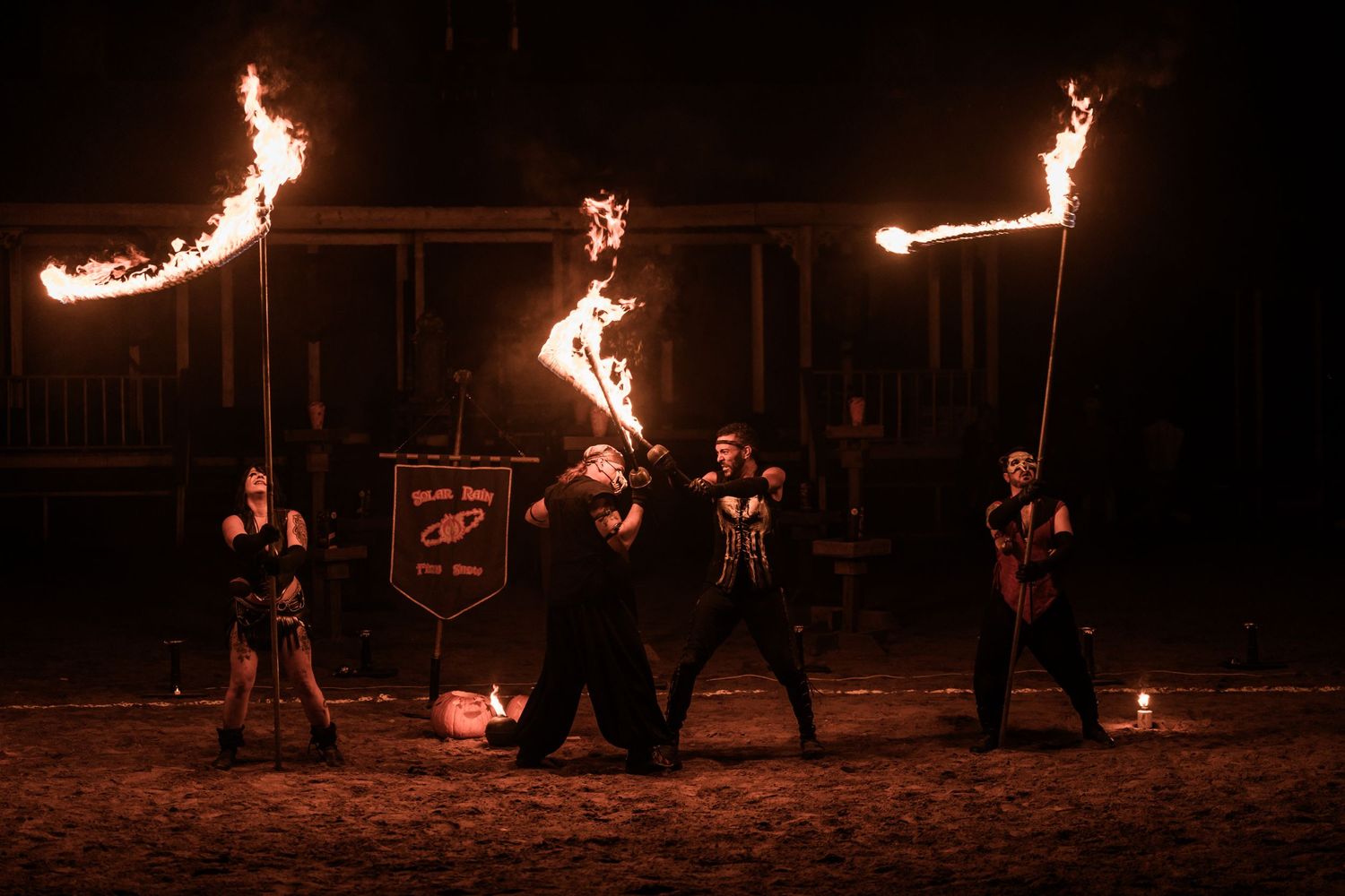 Fire performers line up in dark costumes while holding flaming torches against night sky.