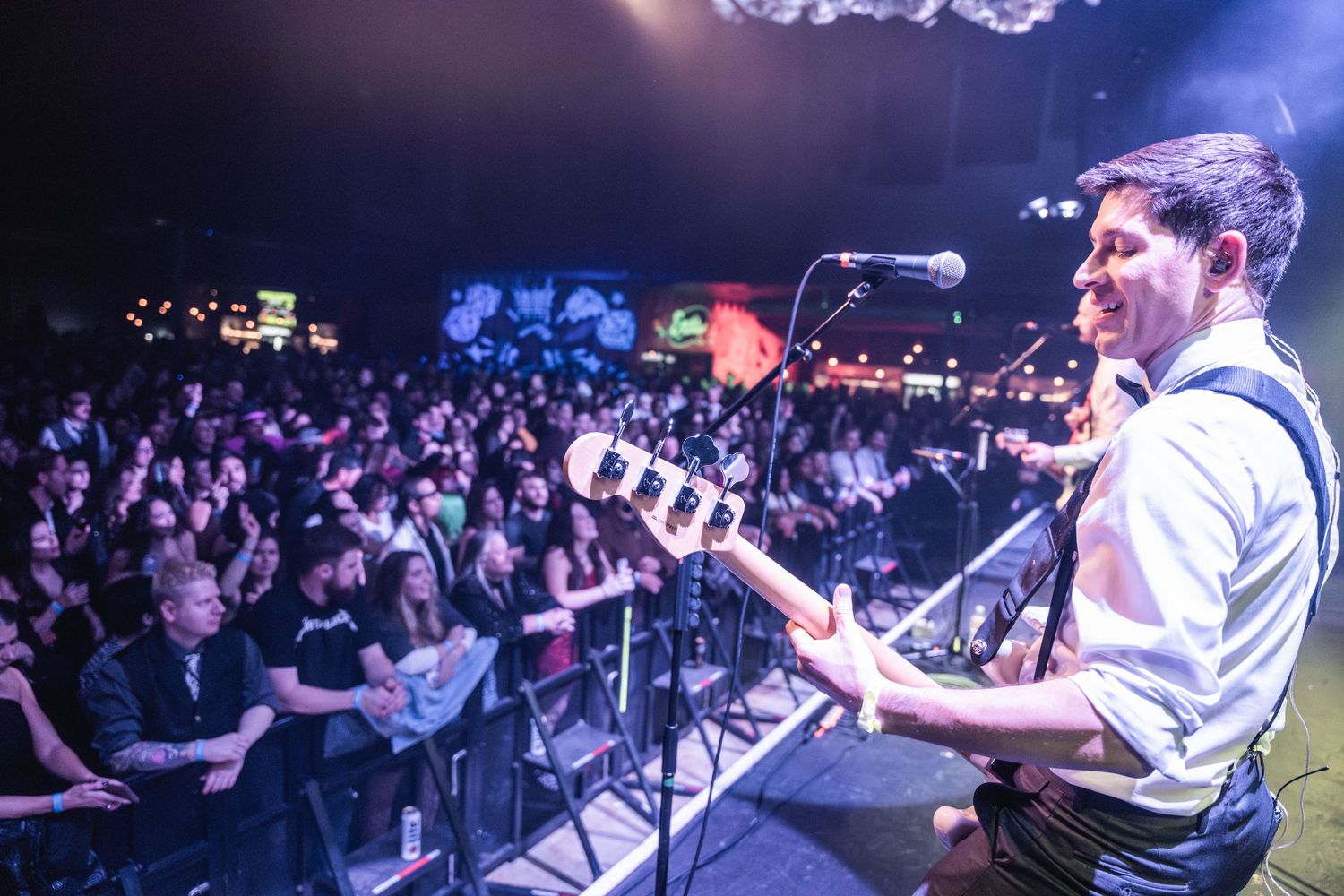 Performer plays guitar on stage overlooking crowd during nighttime concert venue.