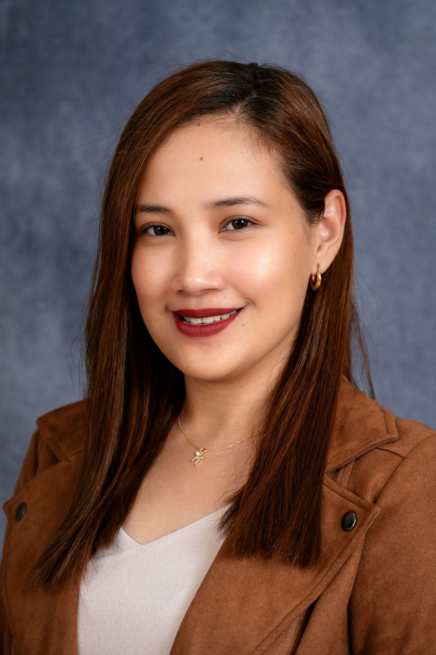 Professional headshot of a person in a brown suede jacket against a gray backdrop.