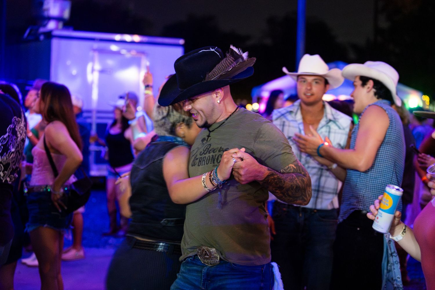 Couples dancing together at a country western bar with neon lights and cowboy hats under dim lighting.