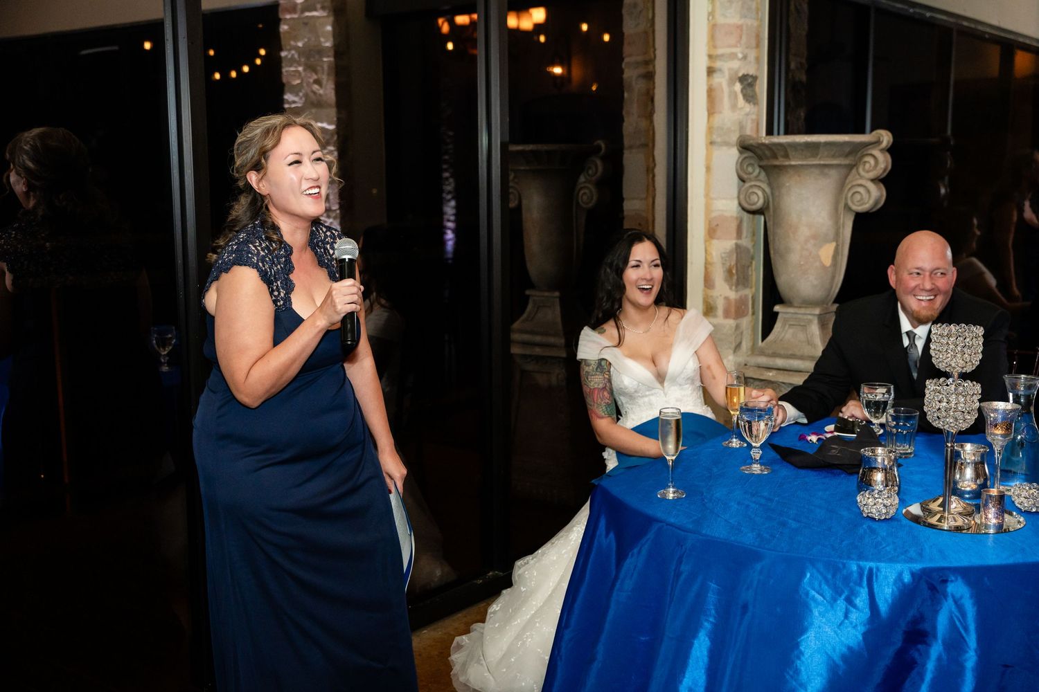 Guest giving a speech during wedding reception with blue tablecloth decor.
