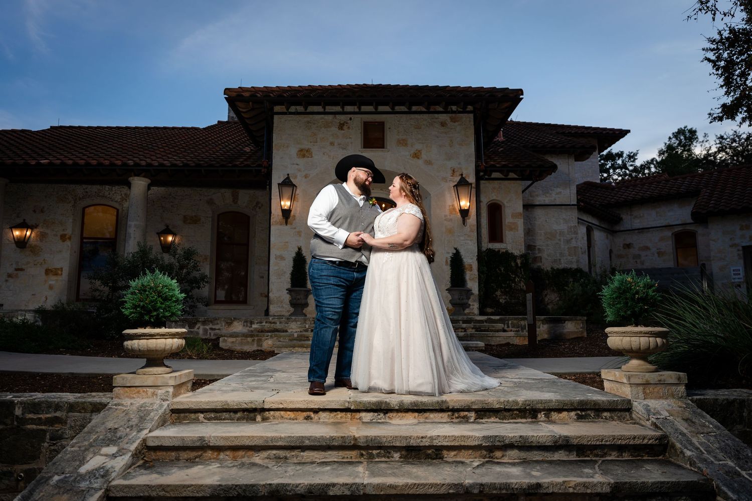 Evening wedding portrait of couple standing on stone steps in front of a rustic villa.
