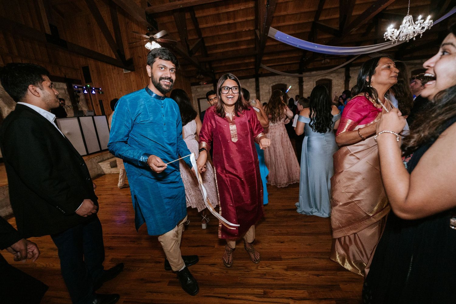 Wedding guests dancing and celebrating on a wooden dance floor decorated with white draping.