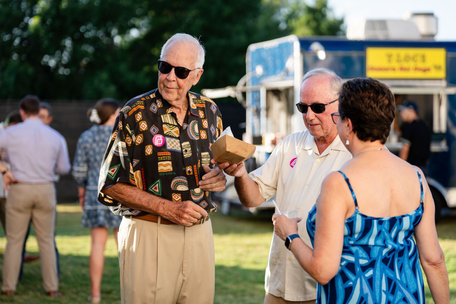 People enjoying refreshments at an outdoor summer gathering with food trucks visible.